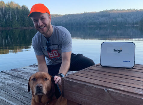 An employee is on a dock located by a lake in a Quebecois landscape. They are using the Strigo device to make a phone call.