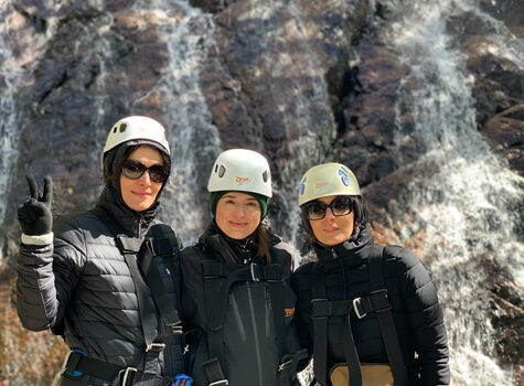 Three employees wearing climbing helmets stand in front of a rocky wall.