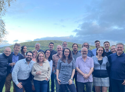 The entire Strigo team is gathered in nature in front of a mountain and a blue sky.